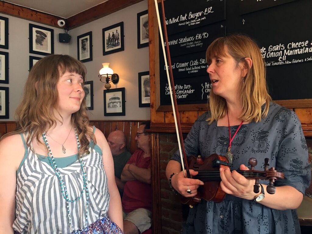 Photograph of Tracey Wisdom playing the fiddle and singing with her daughter, Megan, in the Red Lion pub, Southwold, Suffolk, in 2018